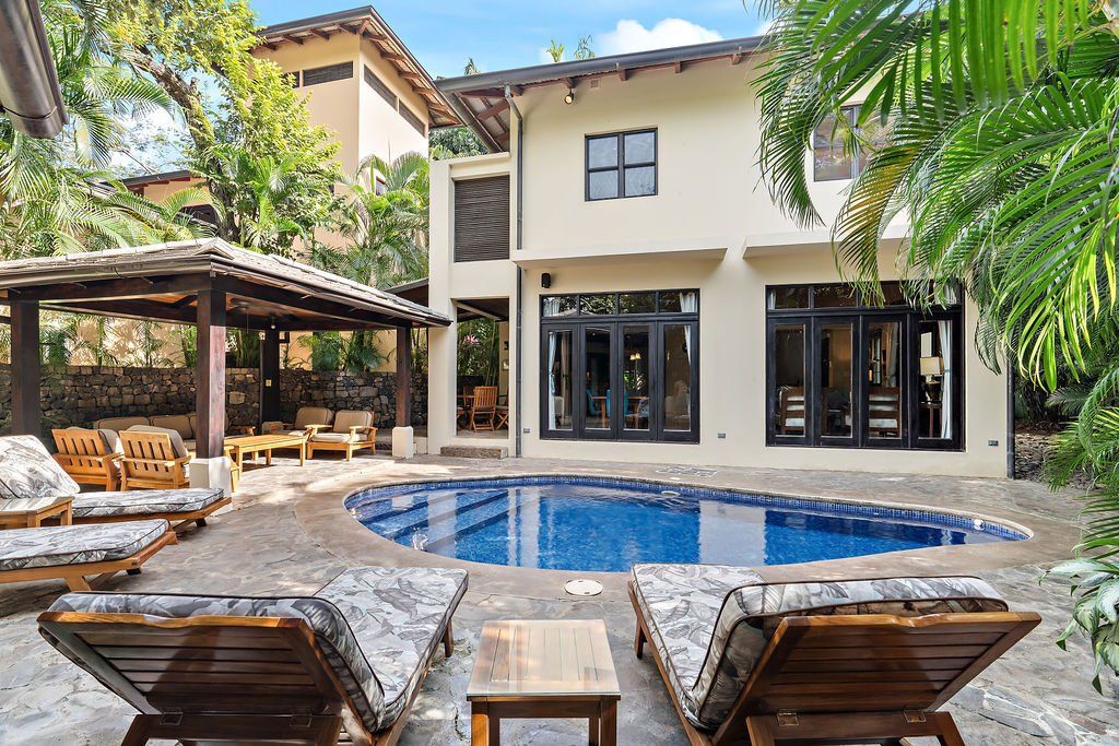 Courtyard villa with a blue pool, lounge chairs, and open patio seating under palm trees