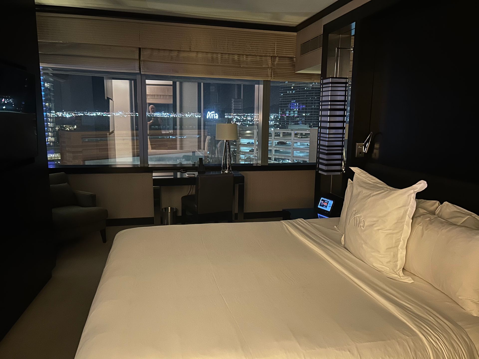 Modern hotel room with a large bed, desk, and city lights visible through the window at night
