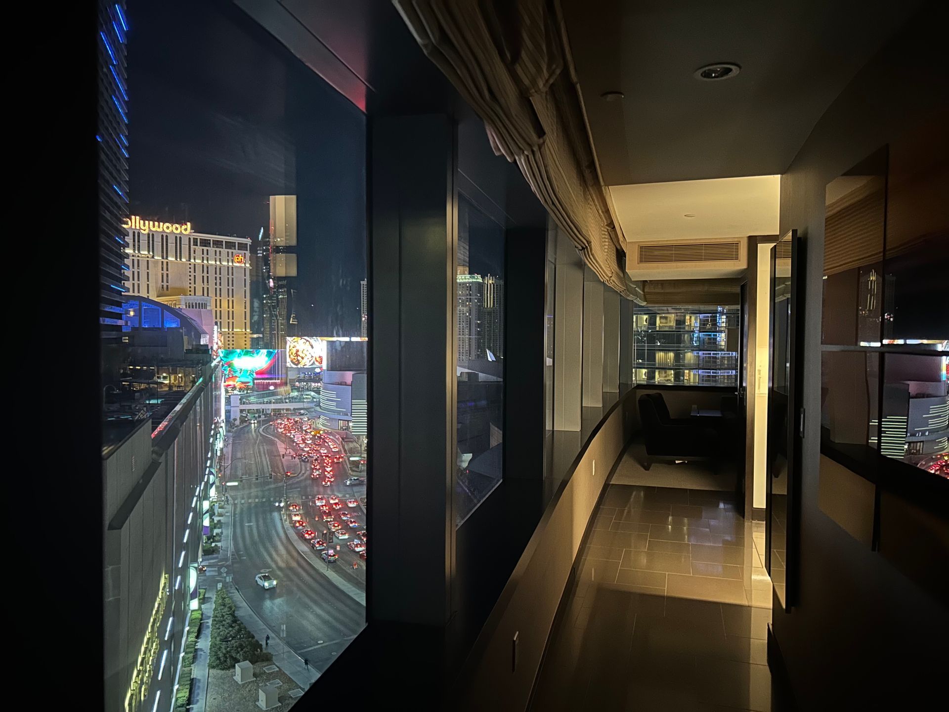 High-rise balcony overlooking a rainy city street at night, with glowing traffic and building lights.