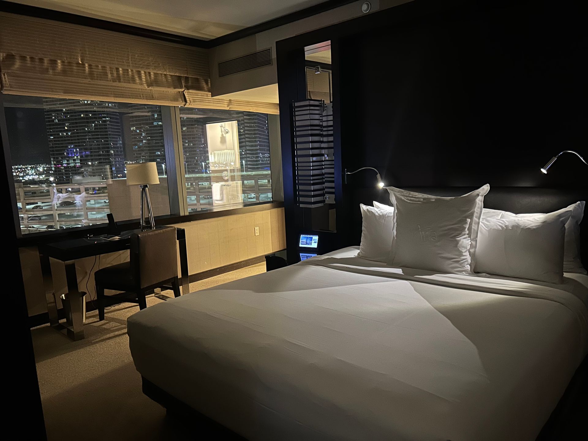 Modern hotel room with a large bed, desk, and city view at night
