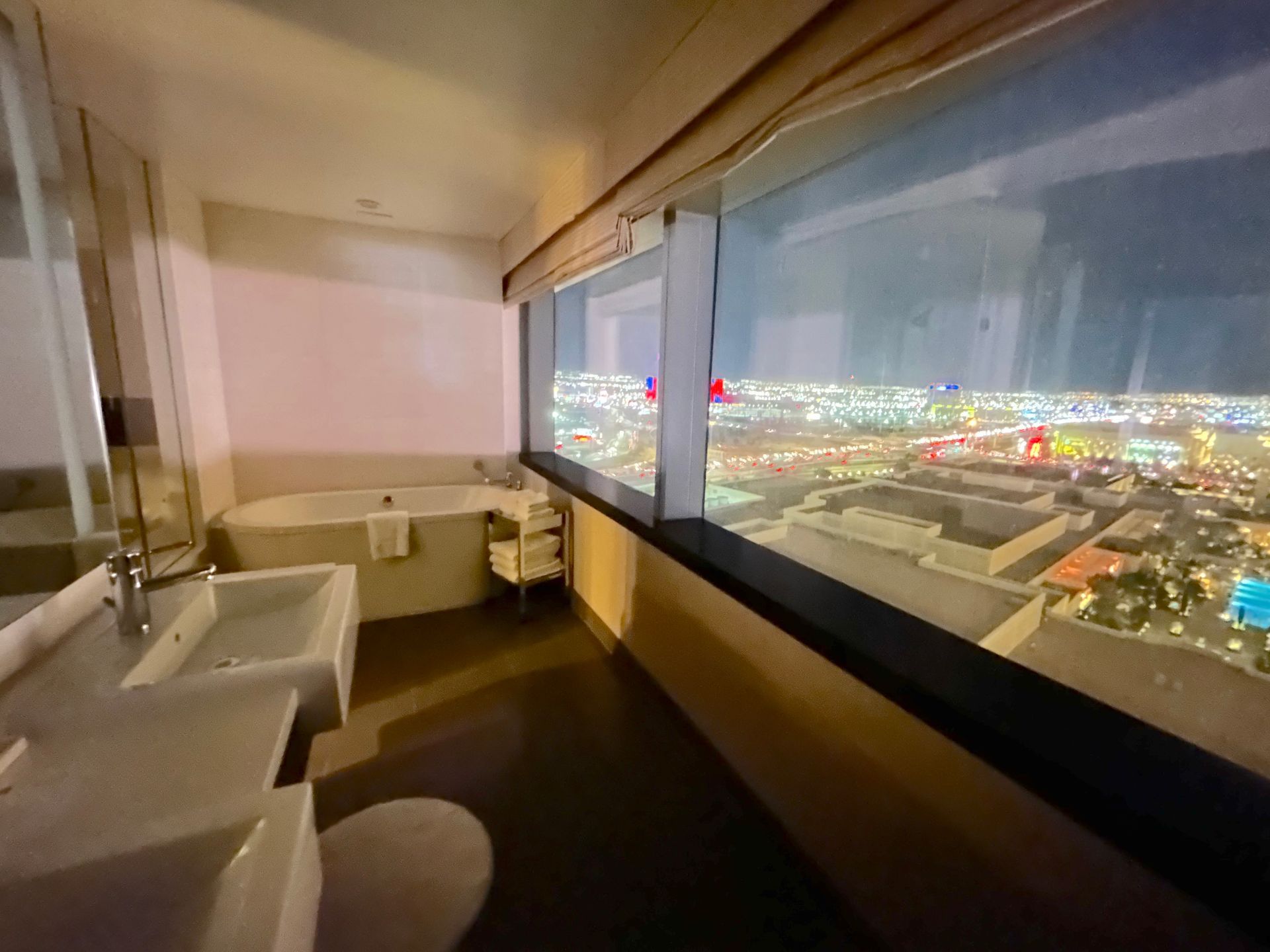 Modern hotel room with large window overlooking a bright city skyline at night