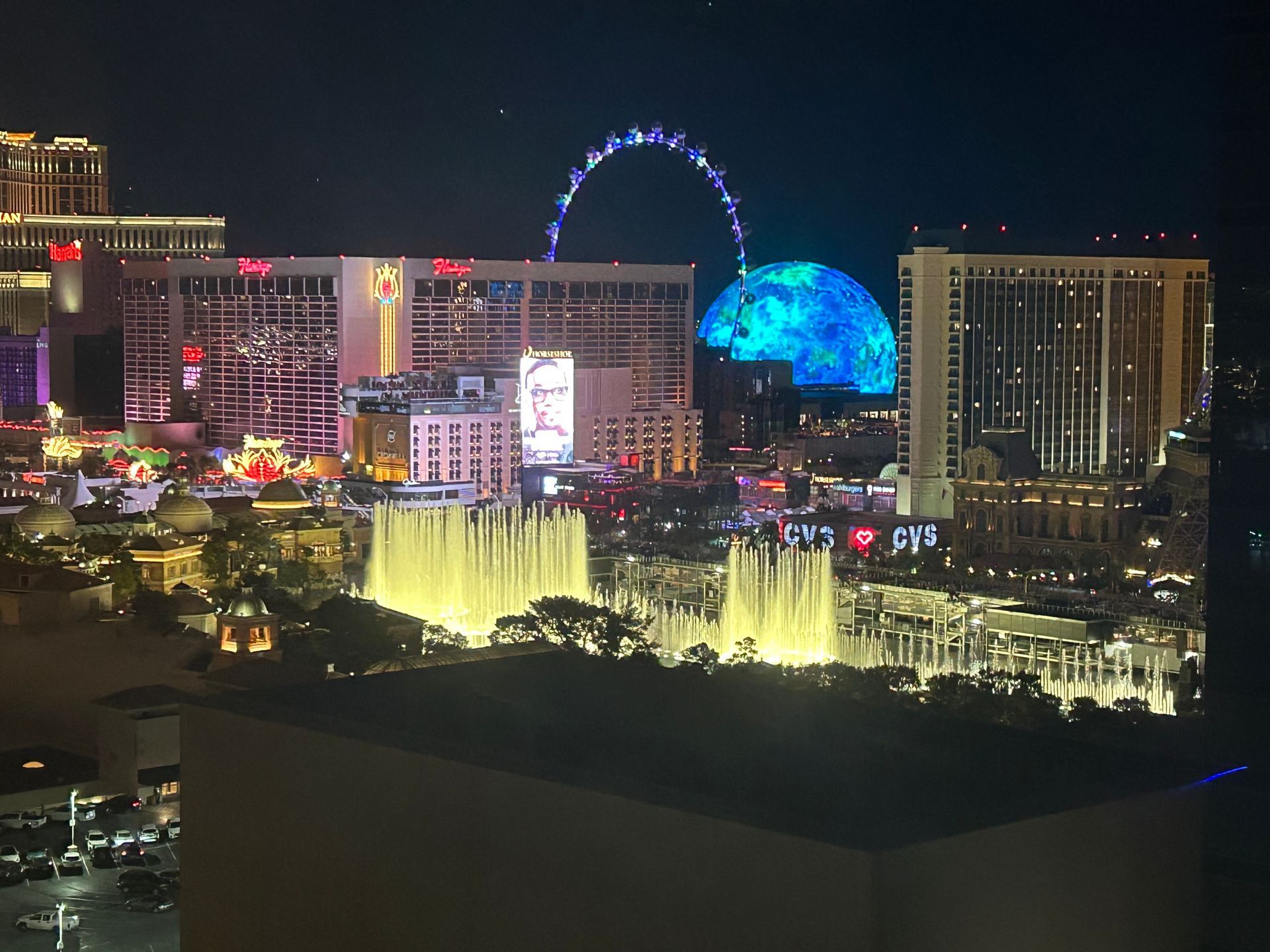 Las Vegas Strip at night with neon-lit hotels, the High Roller, and the illuminated Bellagio fountains.