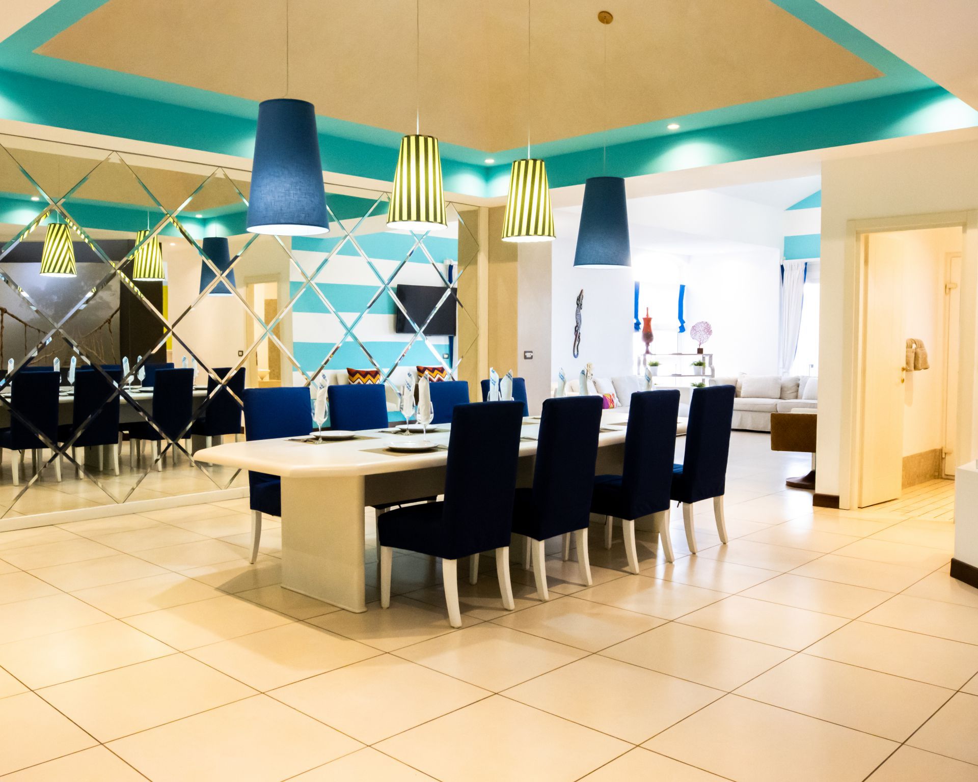 Modern dining room with white table, black chairs, blue pendant lights, and mirrored wall panels