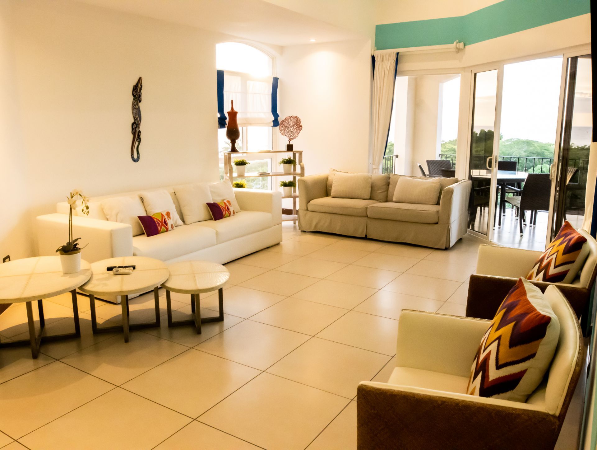 Bright living room with beige sofas, round tables, tiled floor, and large sliding glass doors to a patio.