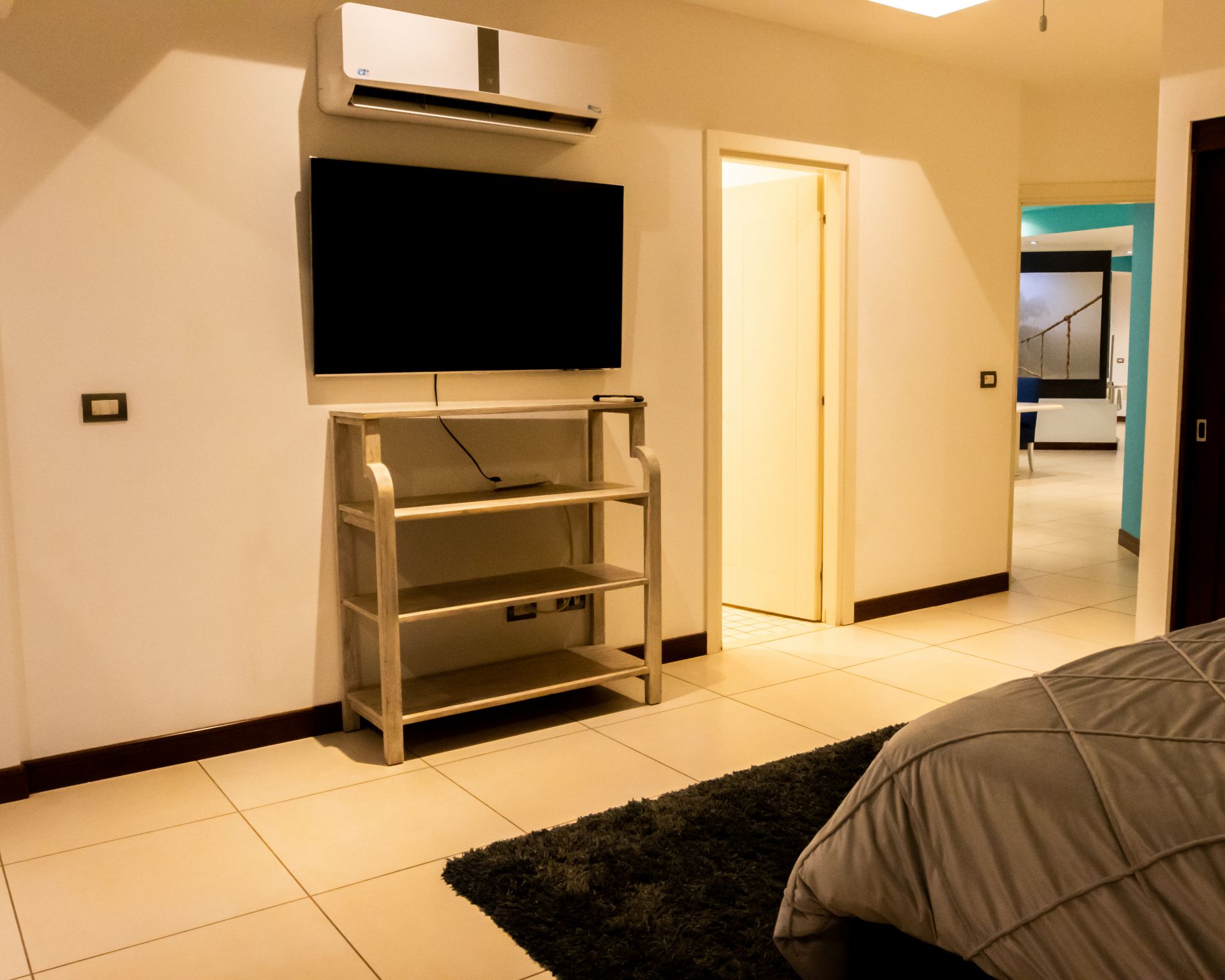 Modern bedroom with wall-mounted TV, air conditioner, metal shelf, and open doorway to hallway.