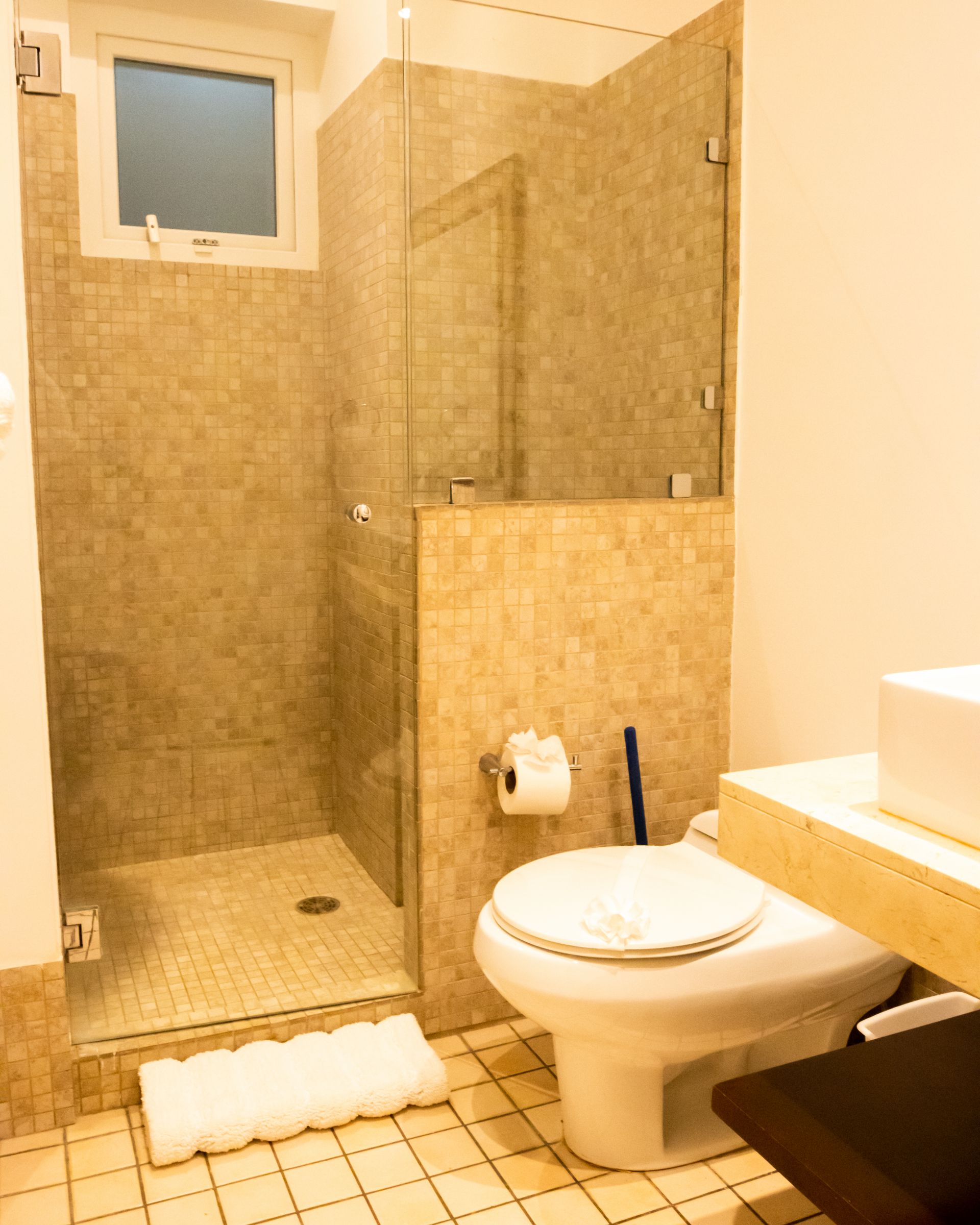 Compact bathroom with tiled shower, toilet, and small window in beige and gray tones