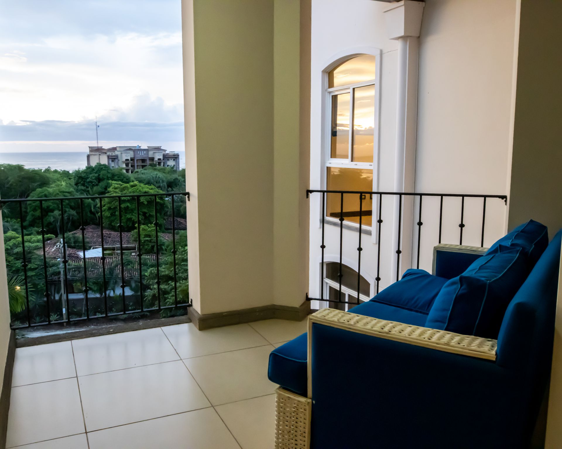 Balcony with blue sofa overlooking green trees and buildings at sunset