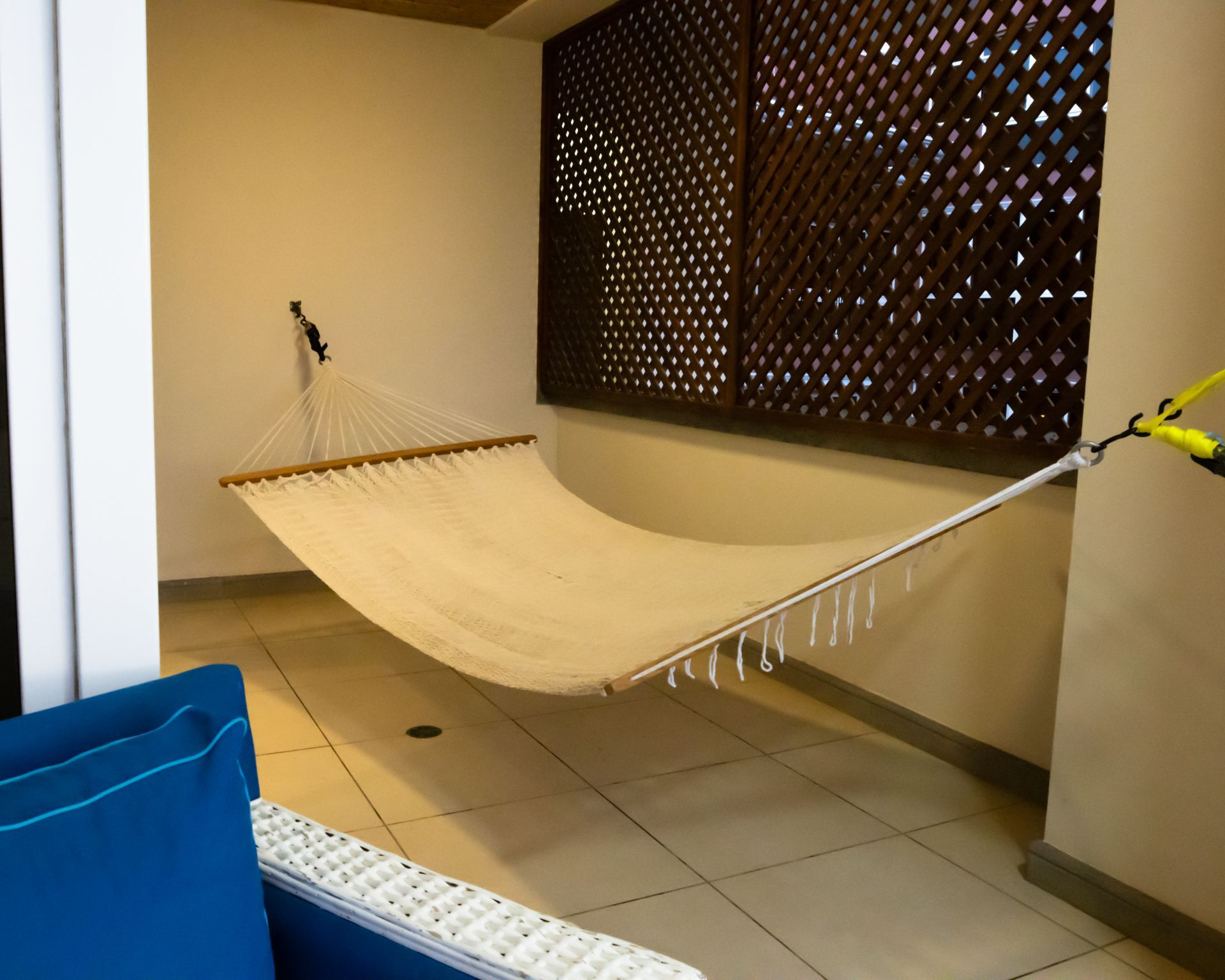 Cream hammock on a tiled balcony beside a blue chair and patterned screen wall.