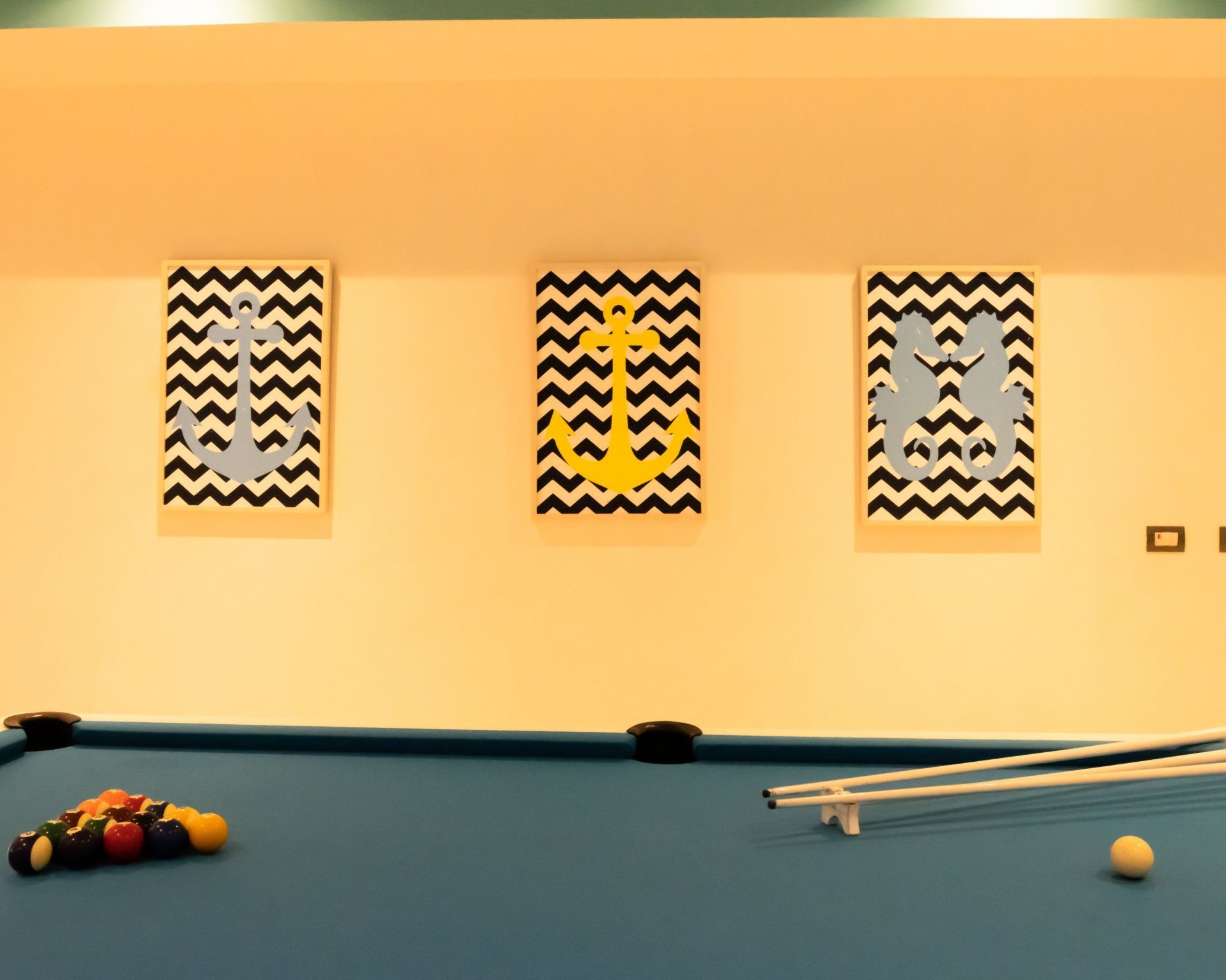 Pool table with scattered balls and cues in a room with three framed geometric wall prints.