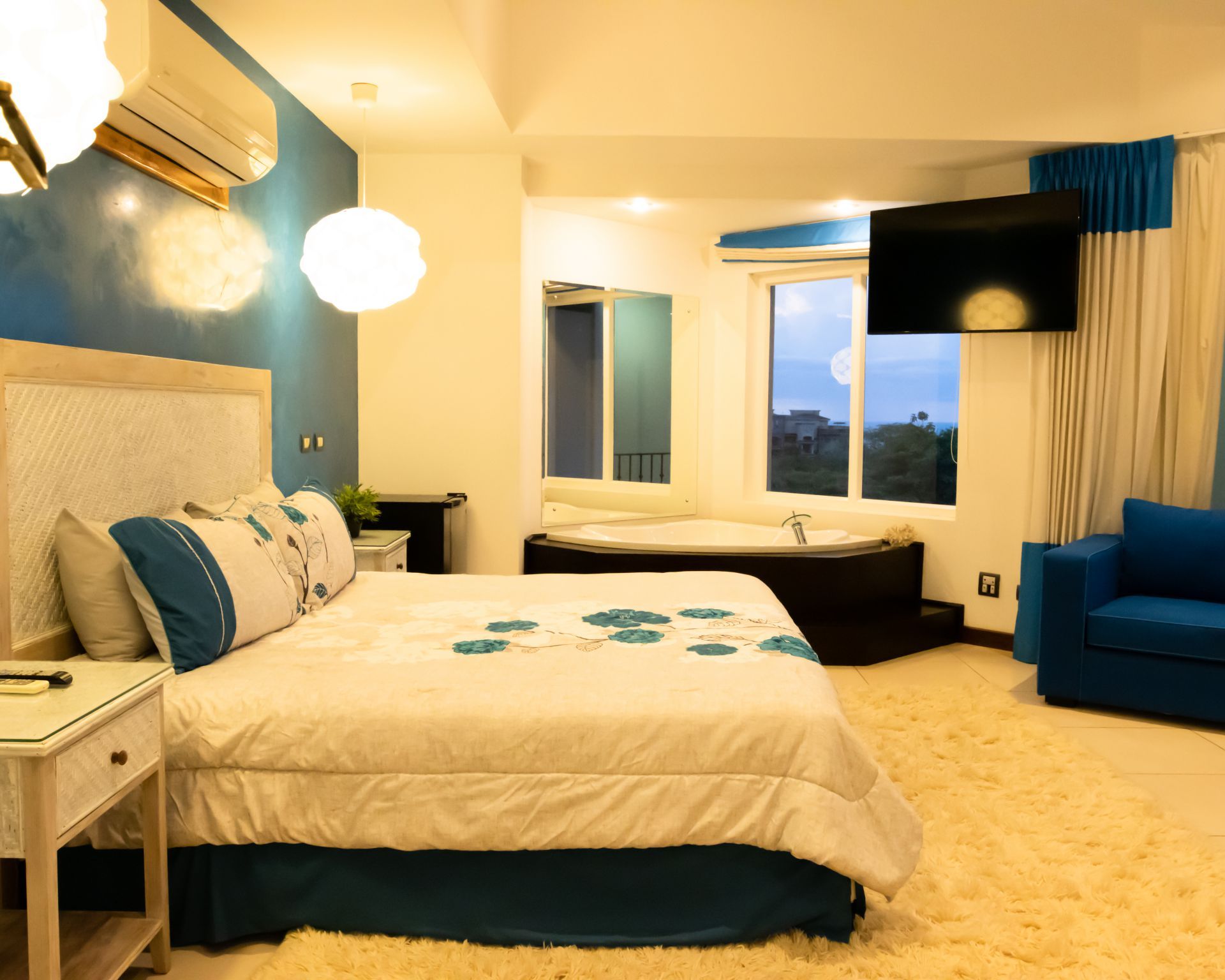 Bright modern hotel room with twin beds, blue accents, window view, and a blue armchair