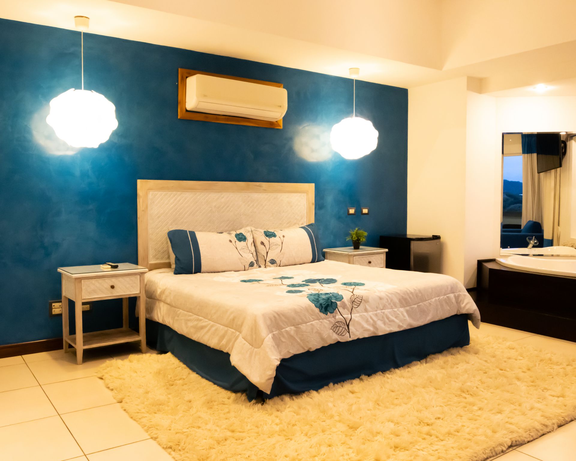 Modern bedroom with blue accent wall, queen bed, bedside tables, pendant lights, and shaggy cream rug