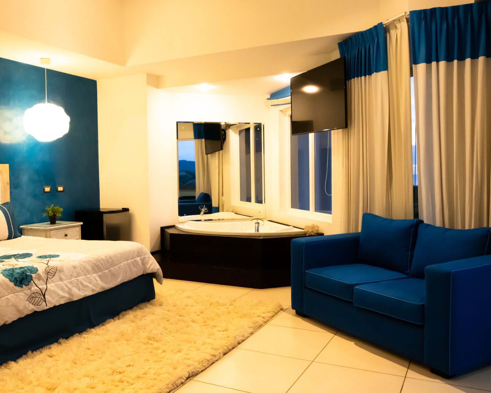 Modern bedroom with blue furnishings, a bed, large mirrors, and floor-to-ceiling curtains