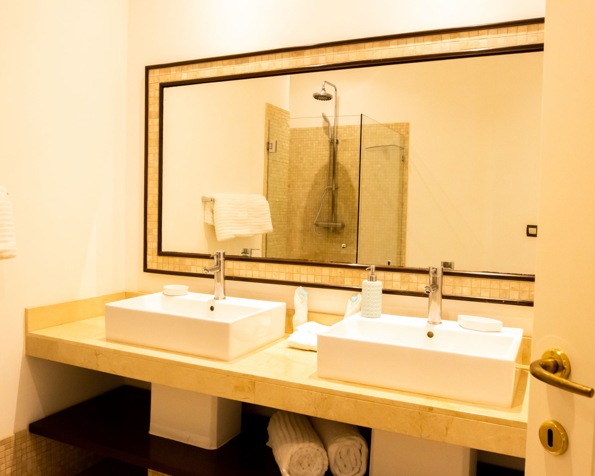 Bathroom vanity with double sinks, large mirror, and warm beige lighting