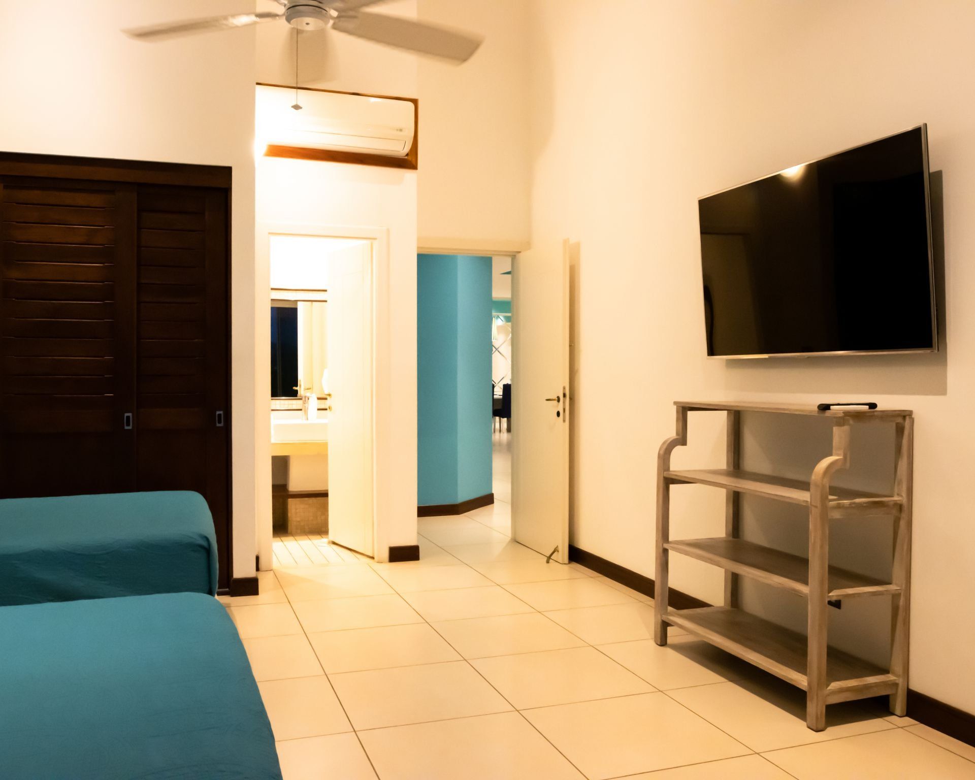 Bedroom with blue bed, dark wardrobe, wall-mounted TV, and open door to a bright hallway