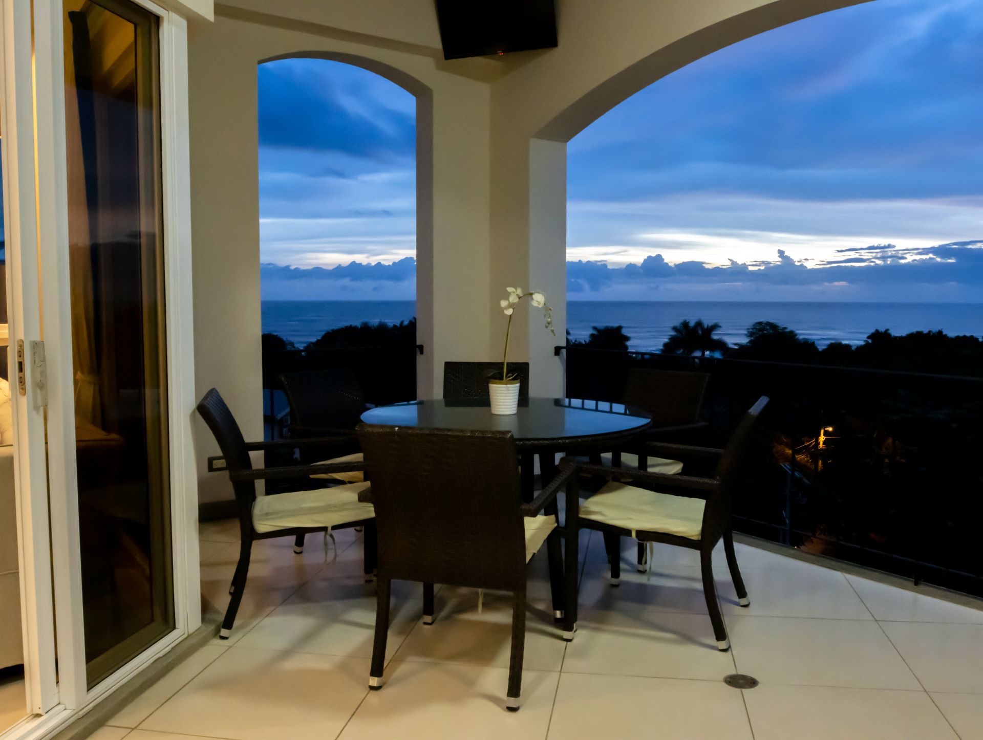 Patio dining table and chairs on a covered terrace at dusk, overlooking a blue sky and distant landscape
