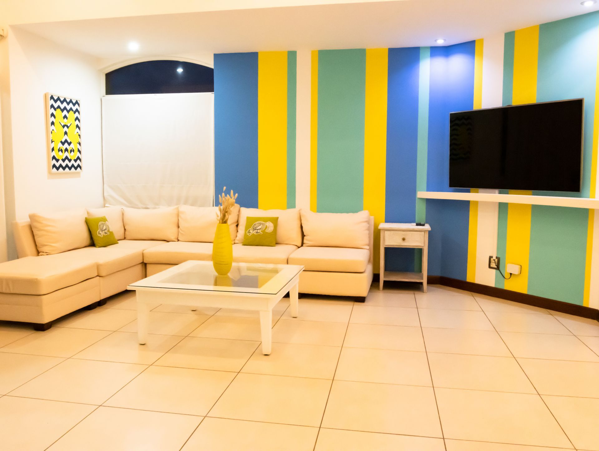 Bright living room with blue and yellow striped walls, beige sectional sofa, white coffee table, and wall-mounted TV