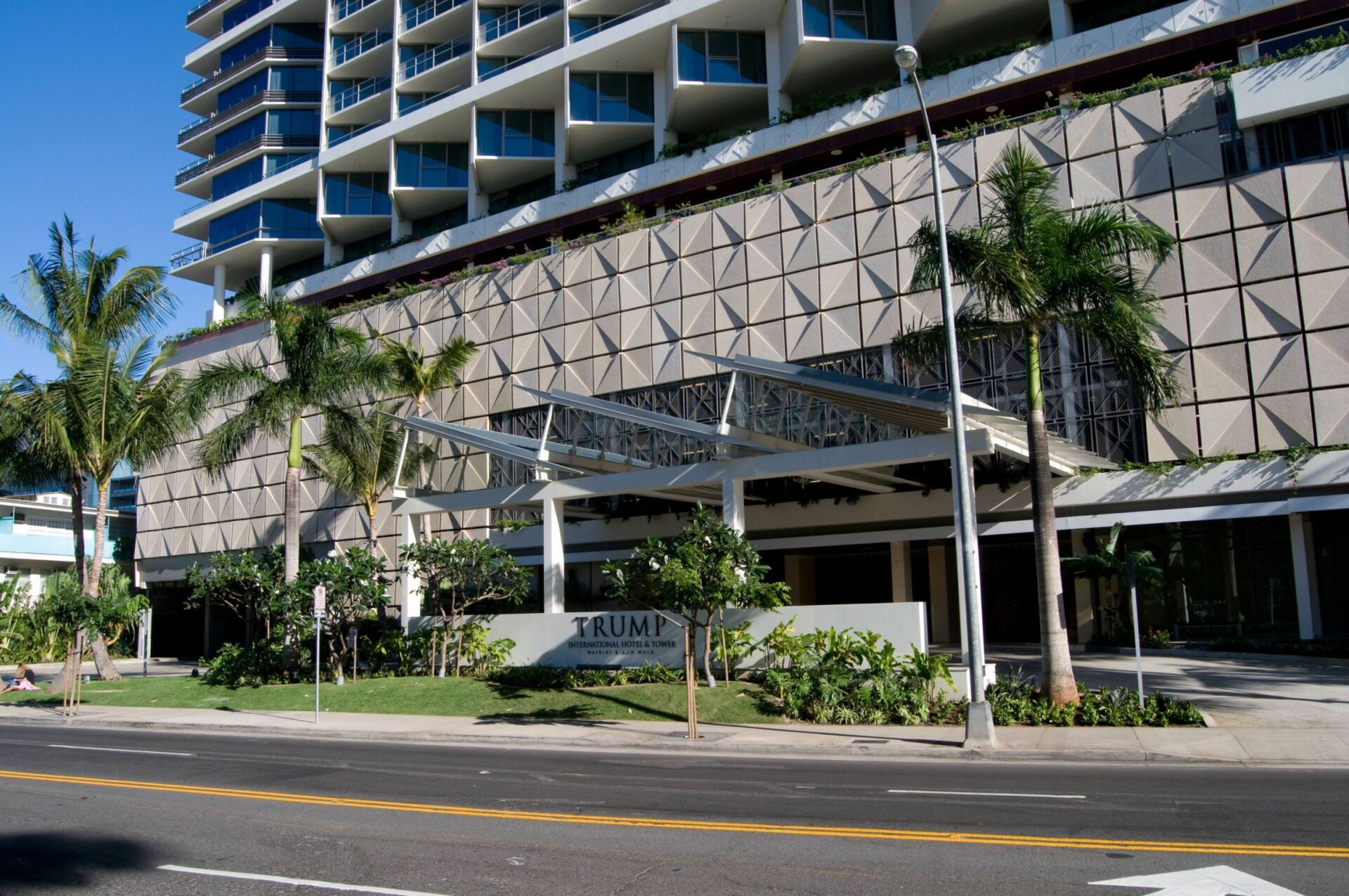 Modern hotel exterior with geometric facade, palm trees, and street view under a clear blue sky