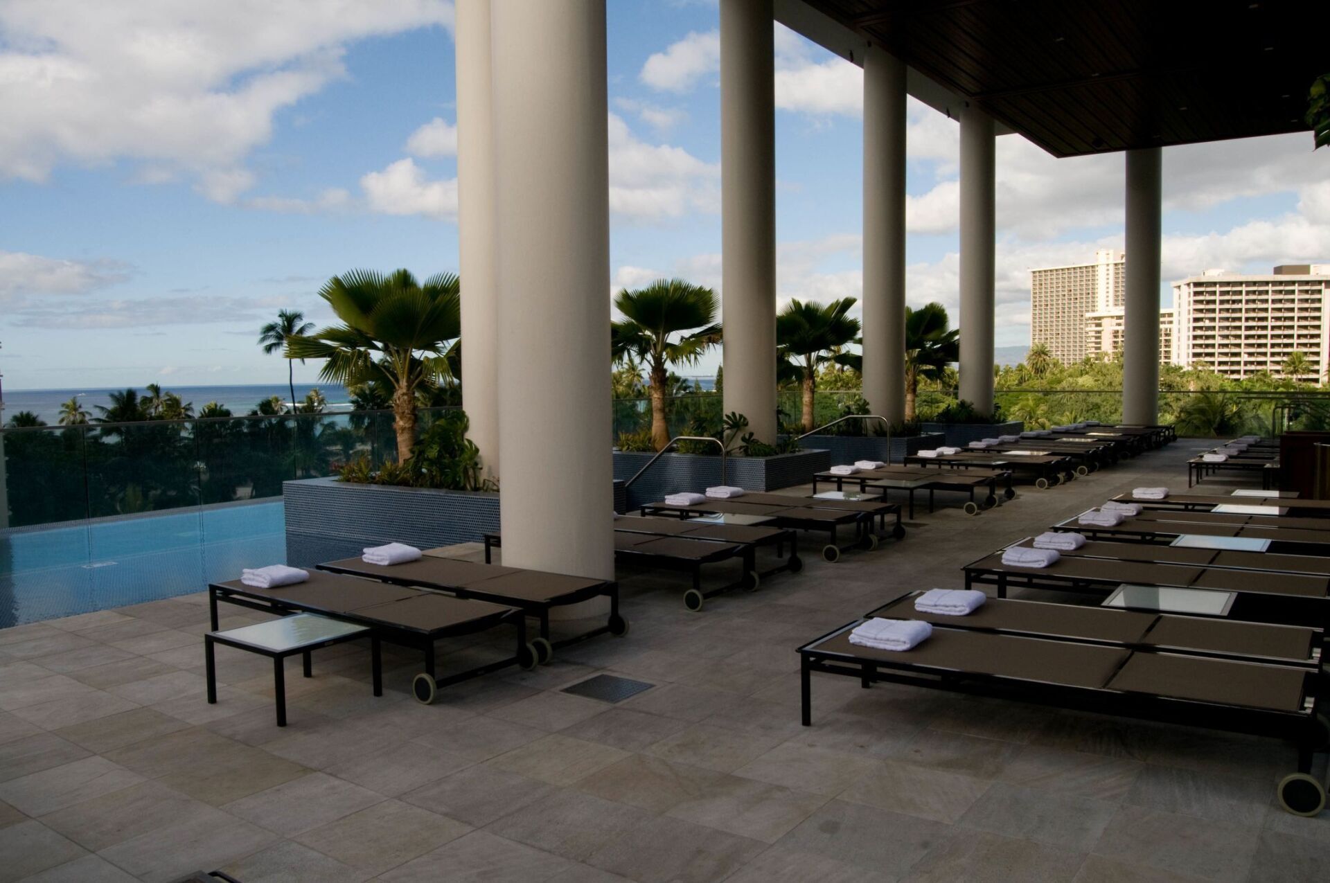 Outdoor pool deck with lounge chairs, white columns, and ocean view at a resort