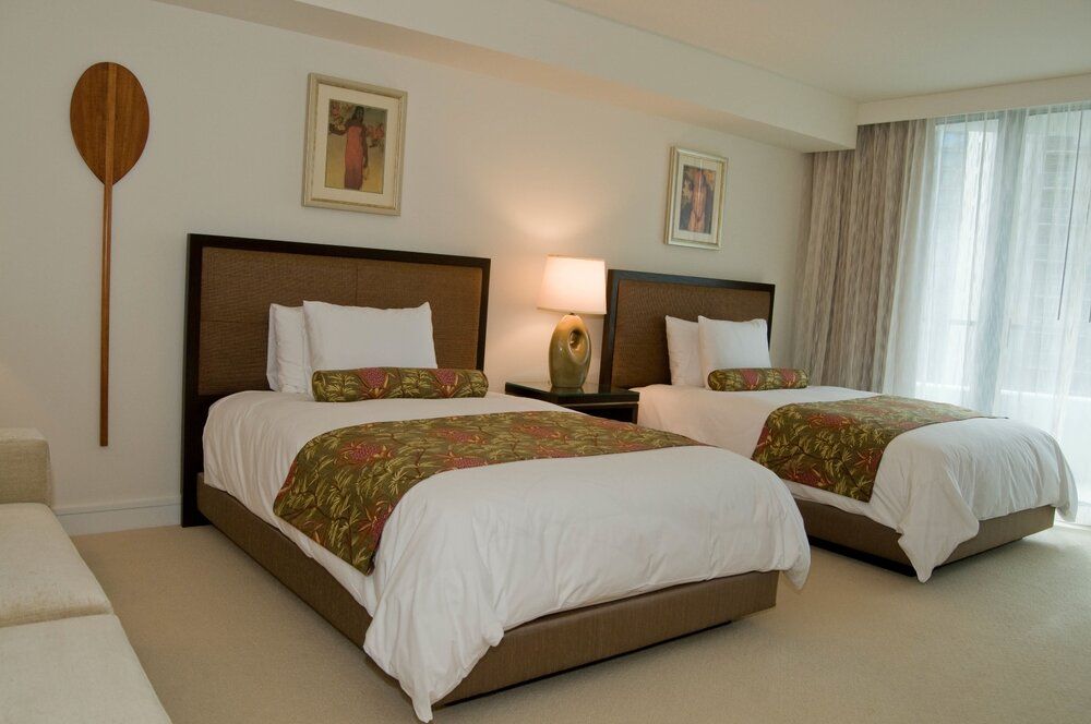Hotel room with two neatly made beds, warm lamps, and a large window with curtains