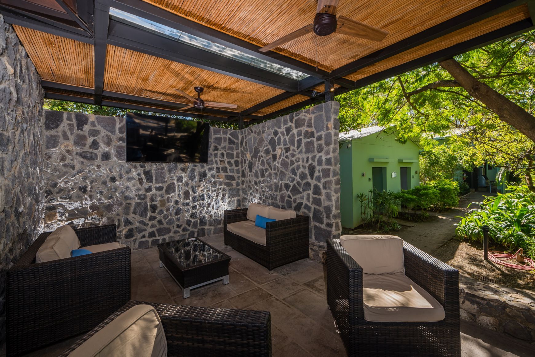 Covered patio with wicker seating, stone walls, TV, and a garden view beyond the open side