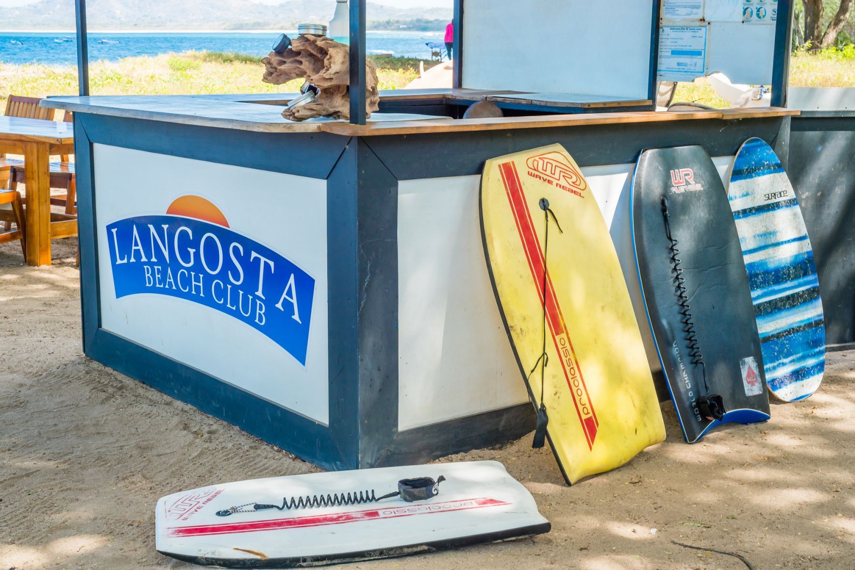 Beachside surfboard rack with colorful boards and a Langosta sign under a shaded hut
