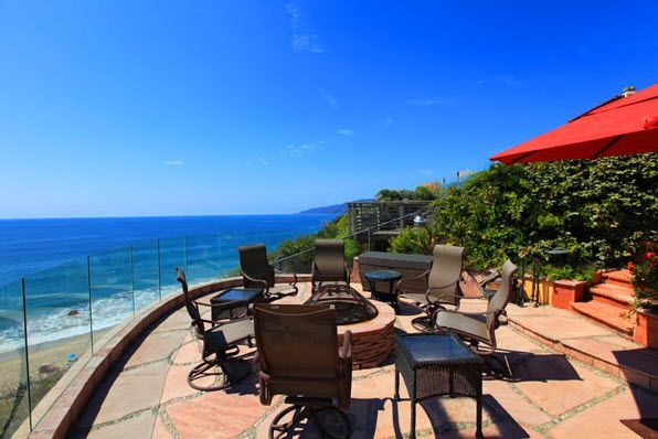 Oceanfront patio with wicker chairs, red umbrella, and a view of the sea and sky