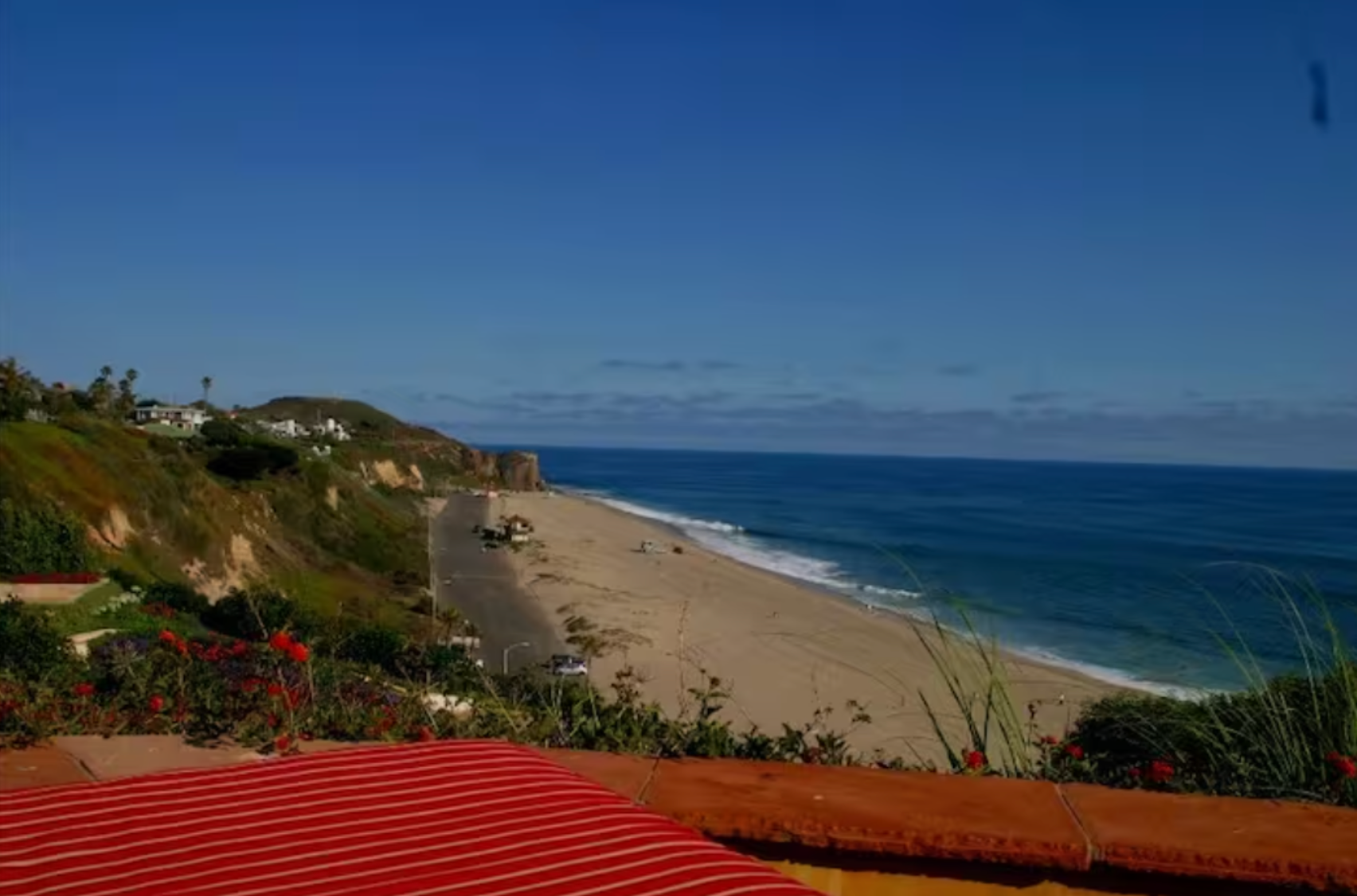 Sunny beach coastline with blue ocean, sandy shore, and red-striped foreground under a clear sky