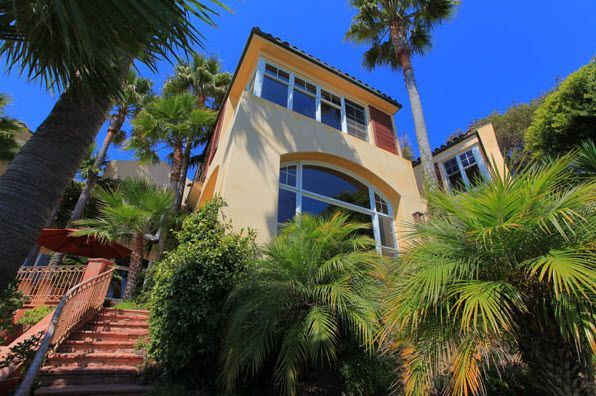Tropical house exterior with beige walls, red stairs, and palm trees under a bright blue sky