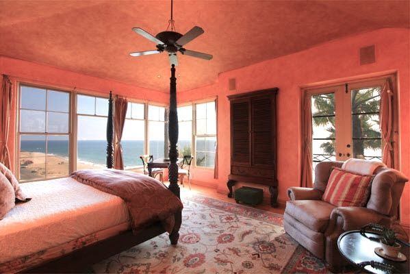 Bedroom with coral walls, large windows, bed, armchair, ceiling fan, and ocean view