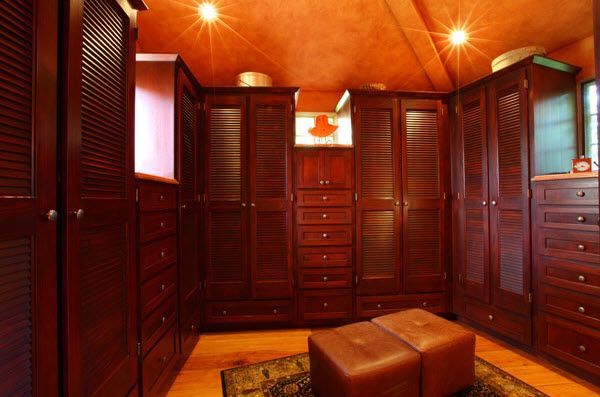 Wood-paneled walk-in closet with drawers, hanging space, and a bench under warm ceiling lights