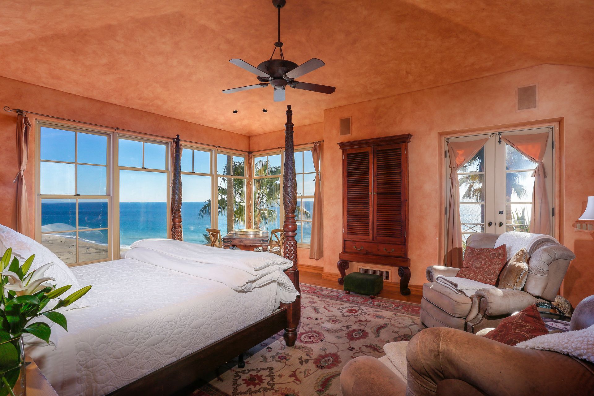 Beachfront bedroom with large windows, ocean view, white bed, and warm orange decor