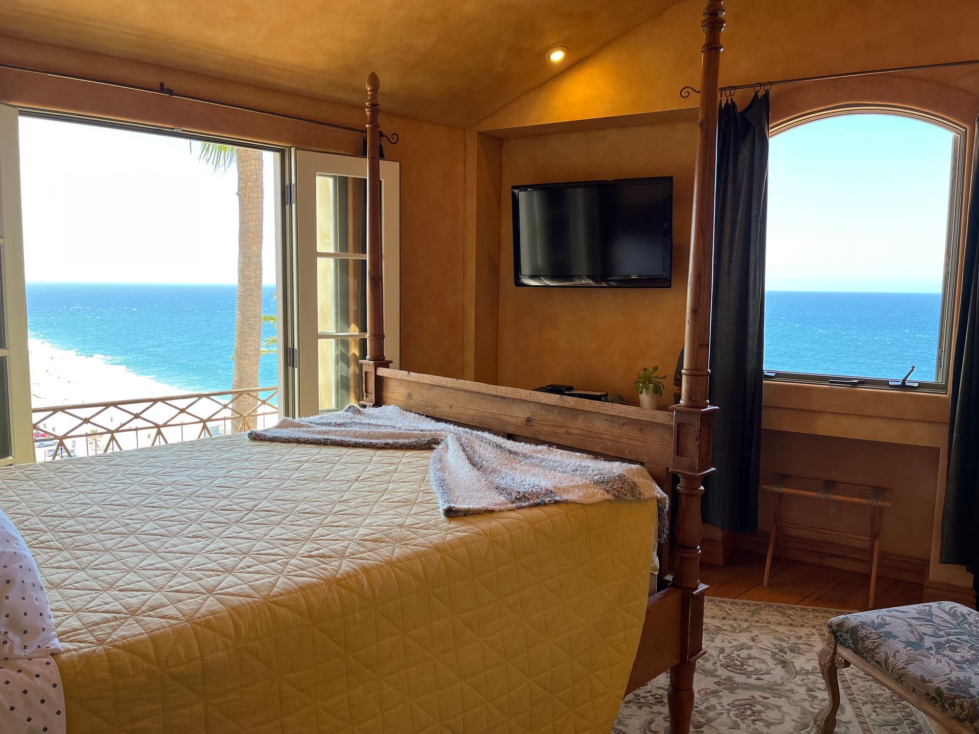 Bedroom with open windows overlooking the ocean and a wall-mounted TV across from the bed