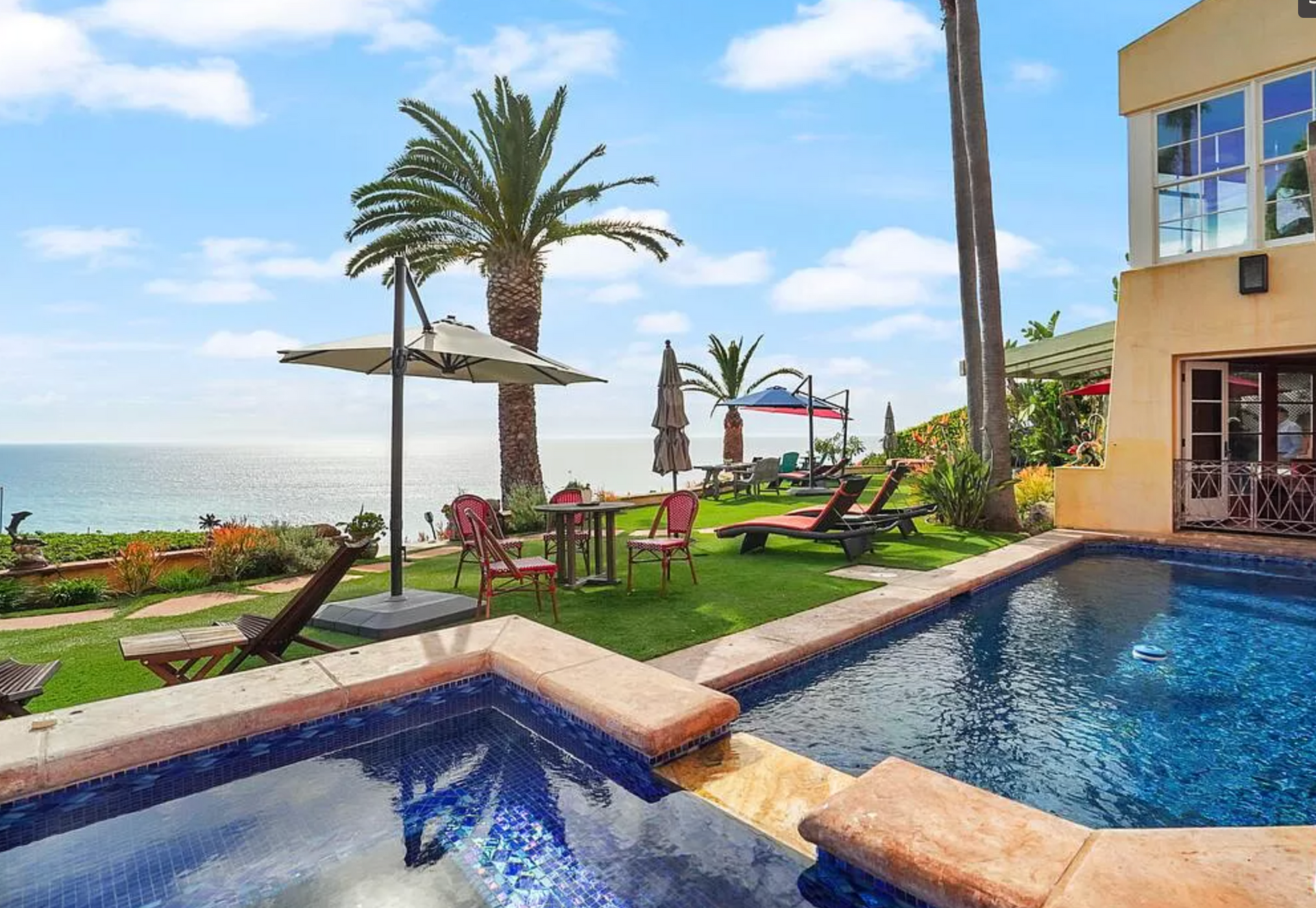 Oceanfront villa with pool, palm trees, lounge chairs, and sea view