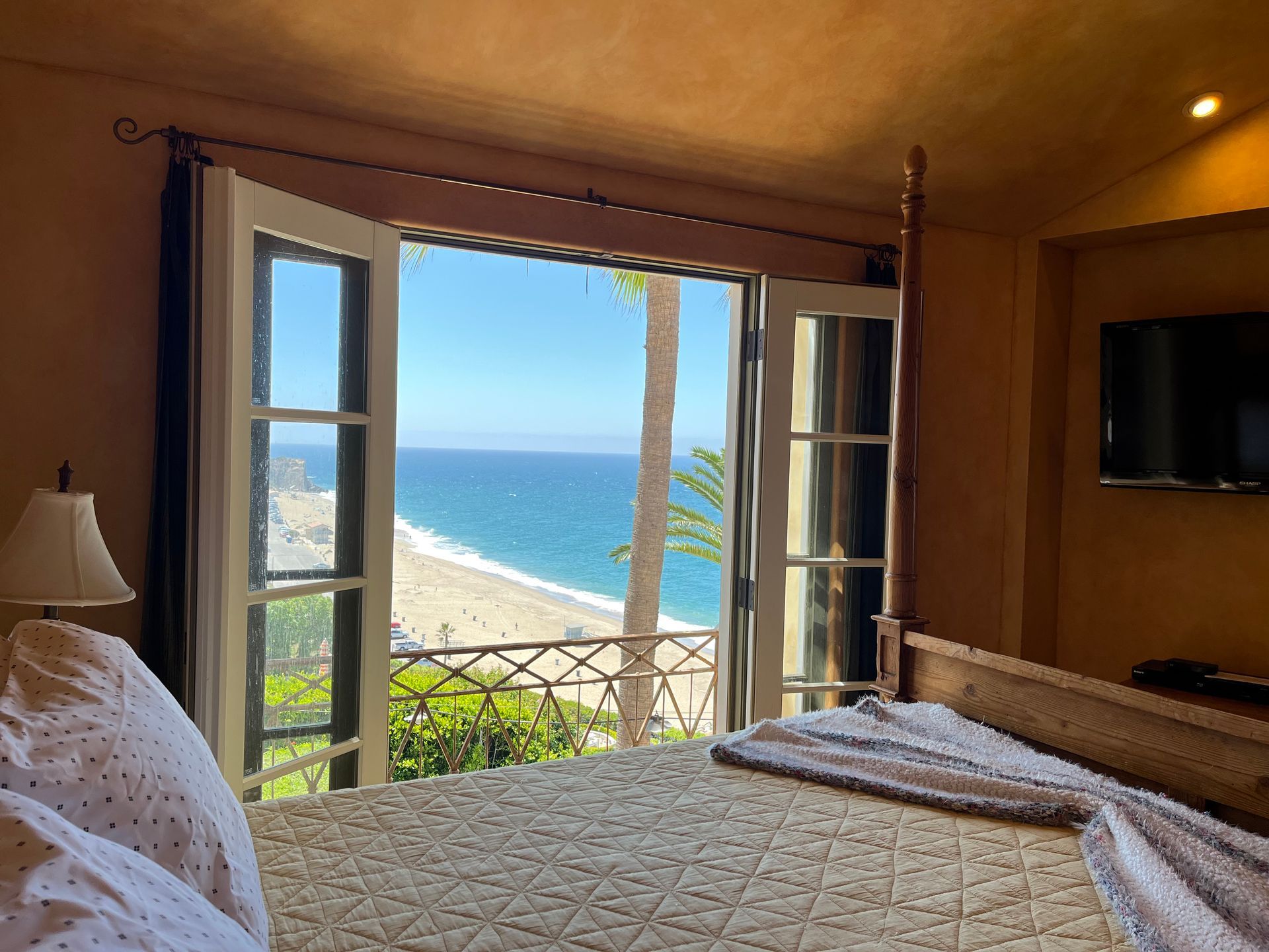 Bedroom with open balcony doors overlooking a bright blue ocean and sandy beach.