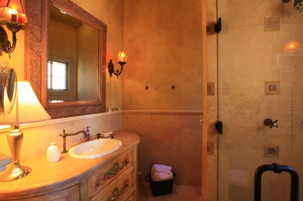 Warm-toned bathroom with a vanity, mirror, sink, wall sconces, and glass shower stall.