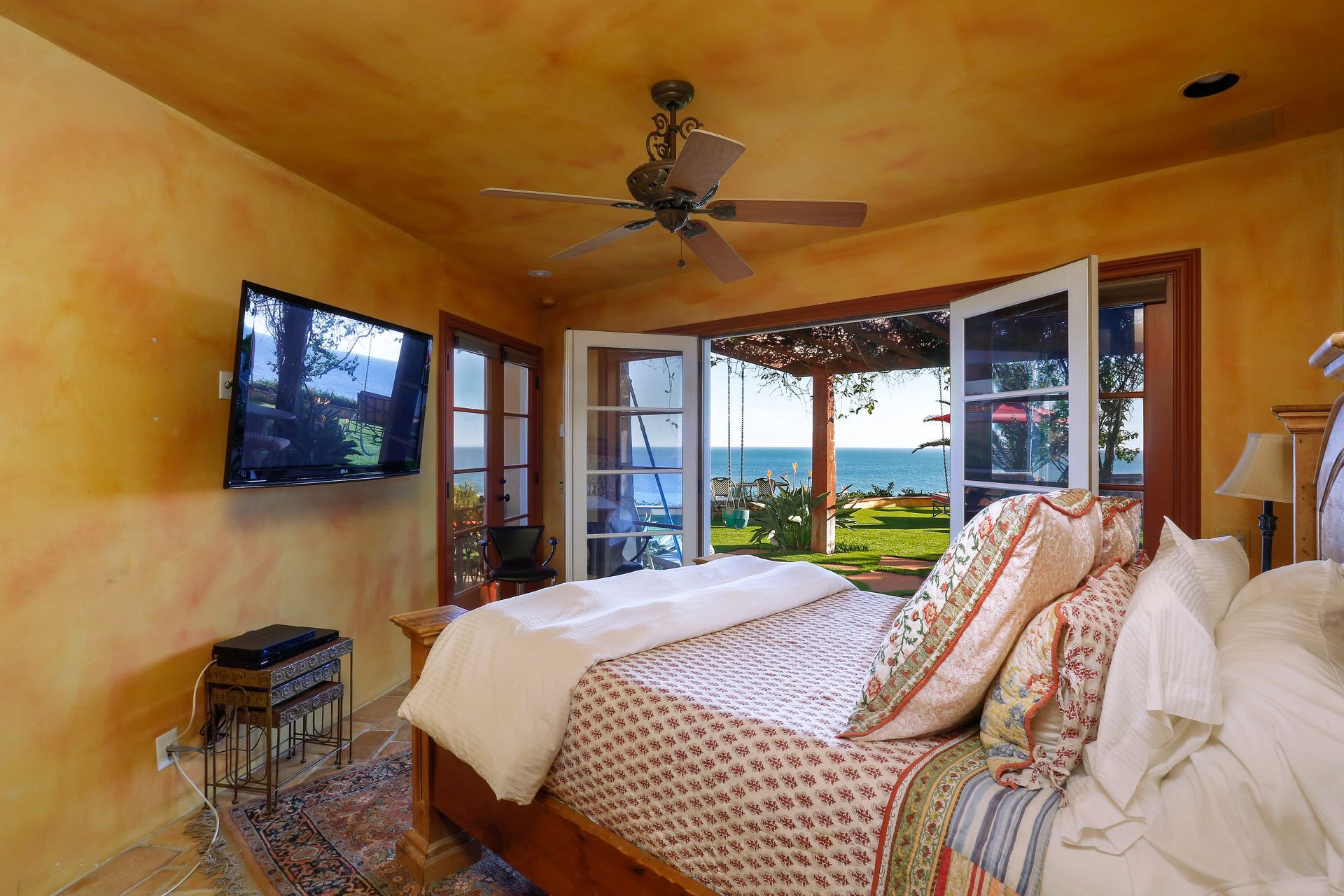 Bedroom with wall TV, ceiling fan, and open doors to a balcony with ocean view.