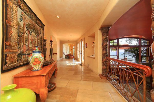 Elegant hallway with art, a vase on a wooden table, and large windows overlooking greenery.