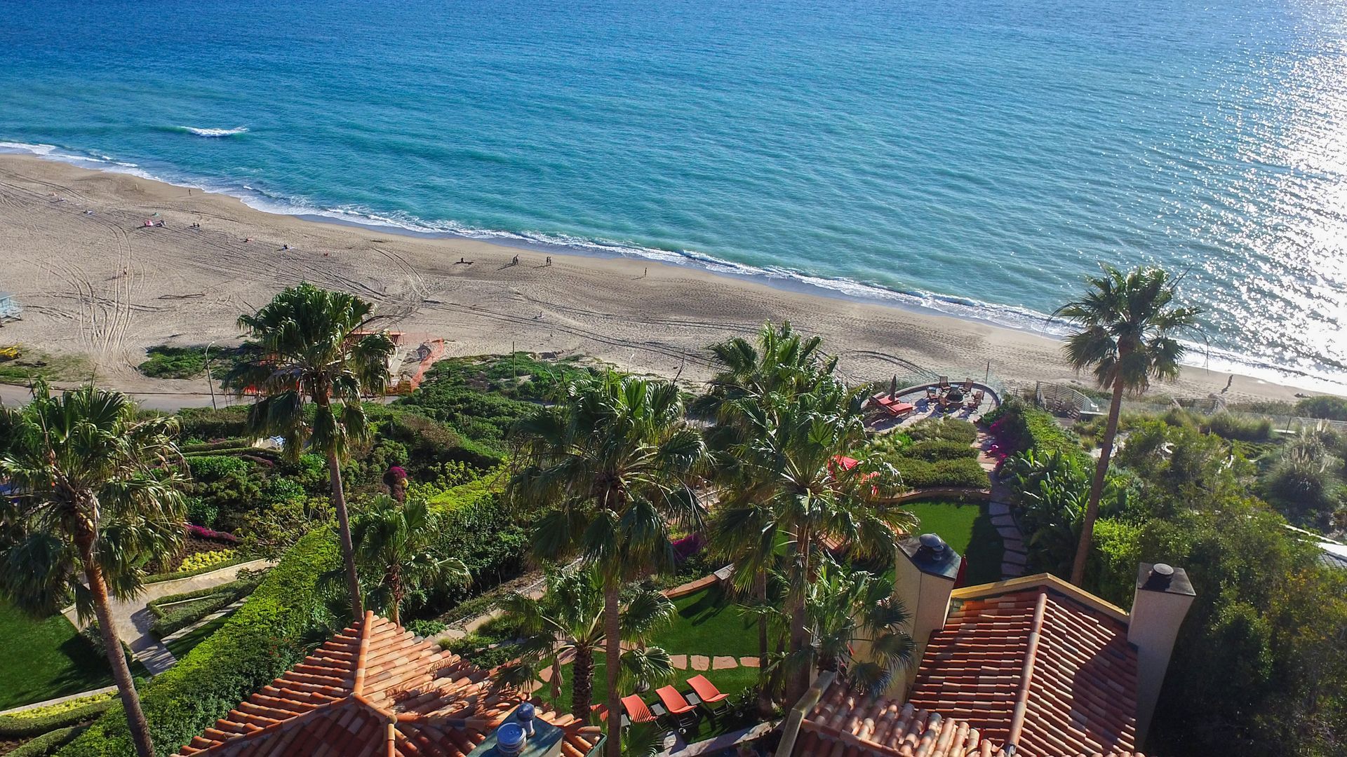 Tropical beach resort view with palm trees, tiled roofs, and turquoise ocean under bright sun
