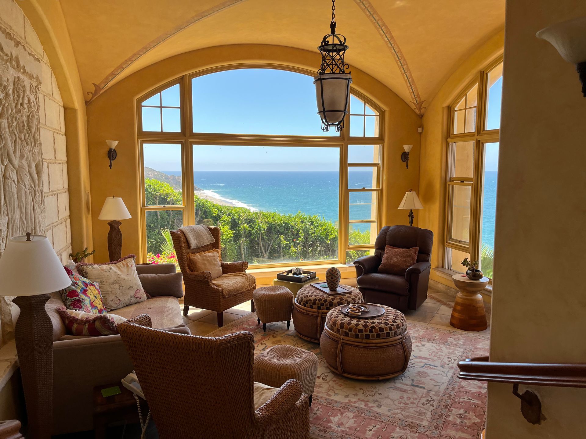 Sunlit ocean-view living room with wicker chairs, arched windows, and warm yellow walls