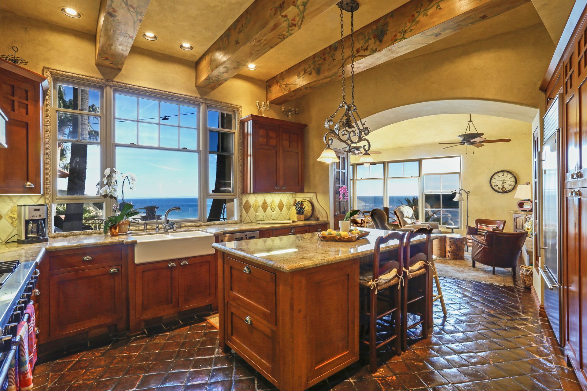 Warm kitchen with large windows, wooden cabinets, island, and adjacent dining area with chandelier.