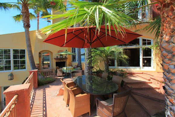 Outdoor patio with wicker seating, red umbrella, and palm trees beside a stucco building