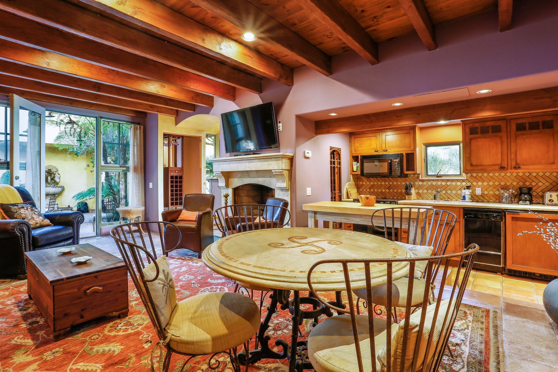 Cozy kitchen and dining room with wood beams, round table, fireplace, and warm wood cabinets