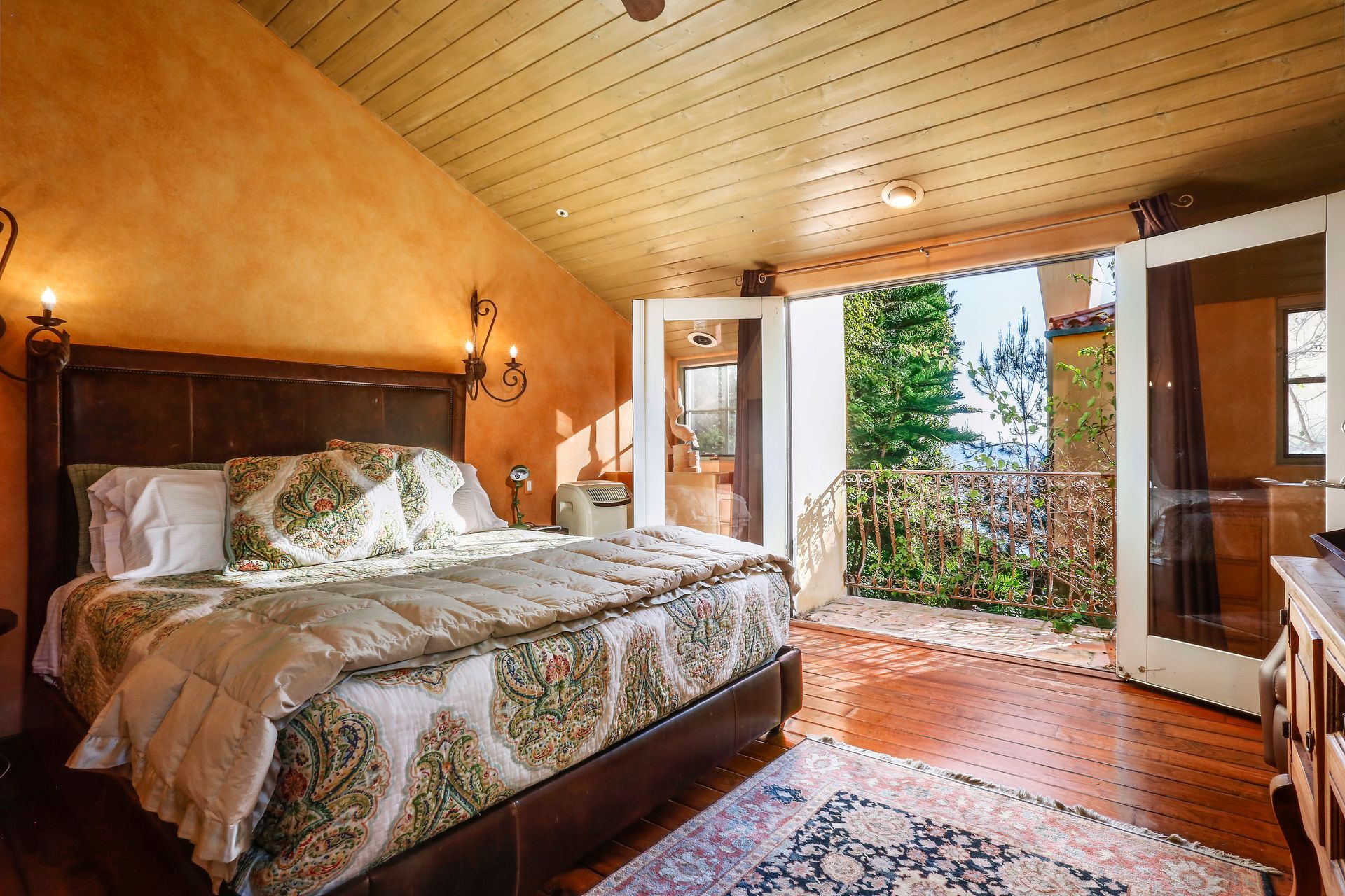 Cozy bedroom with a bed, warm wood ceiling, and open doors to a balcony with a mountain view