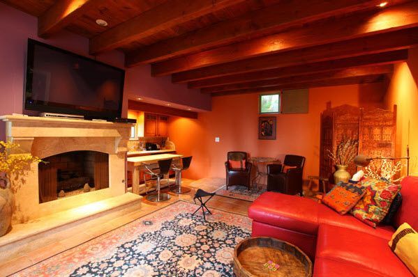 Cozy living room with red sectional, stone fireplace, patterned rug, and warm wood ceiling beams