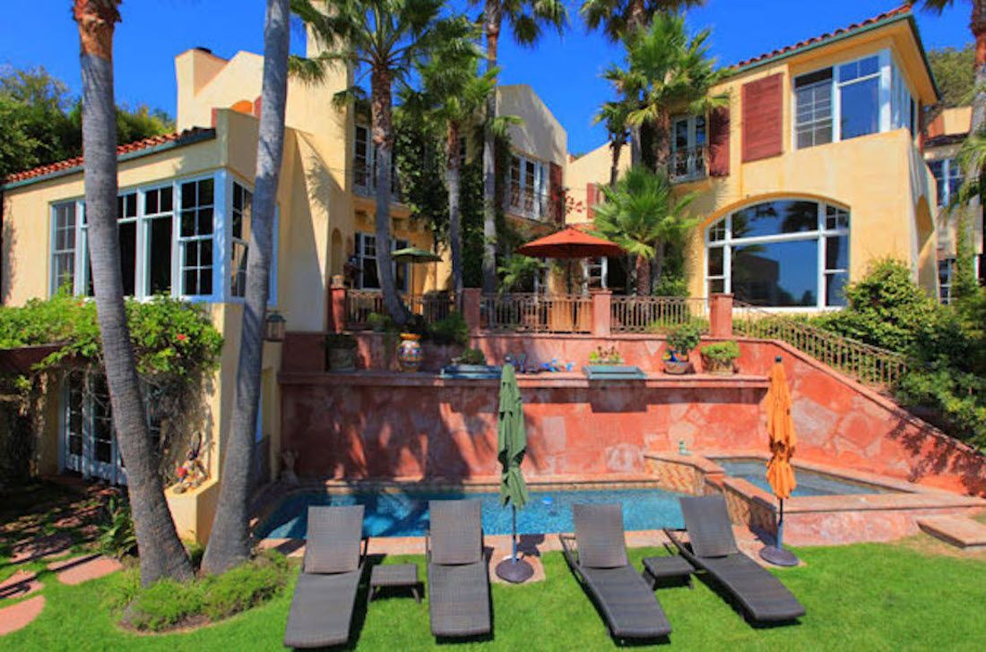 Sunlit luxury villa with palm trees, pool, and lounge chairs on a green lawn