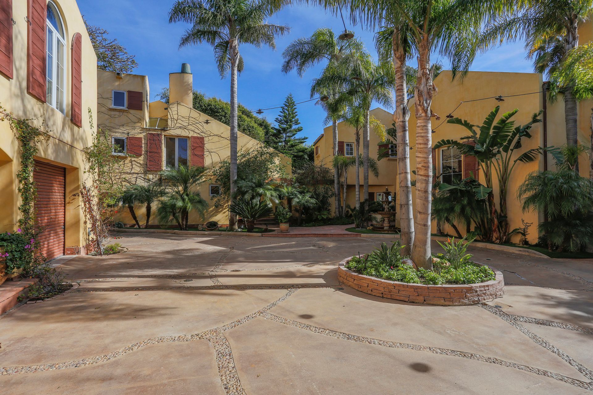Sunny courtyard with tan buildings, palm trees, and patterned stone paving