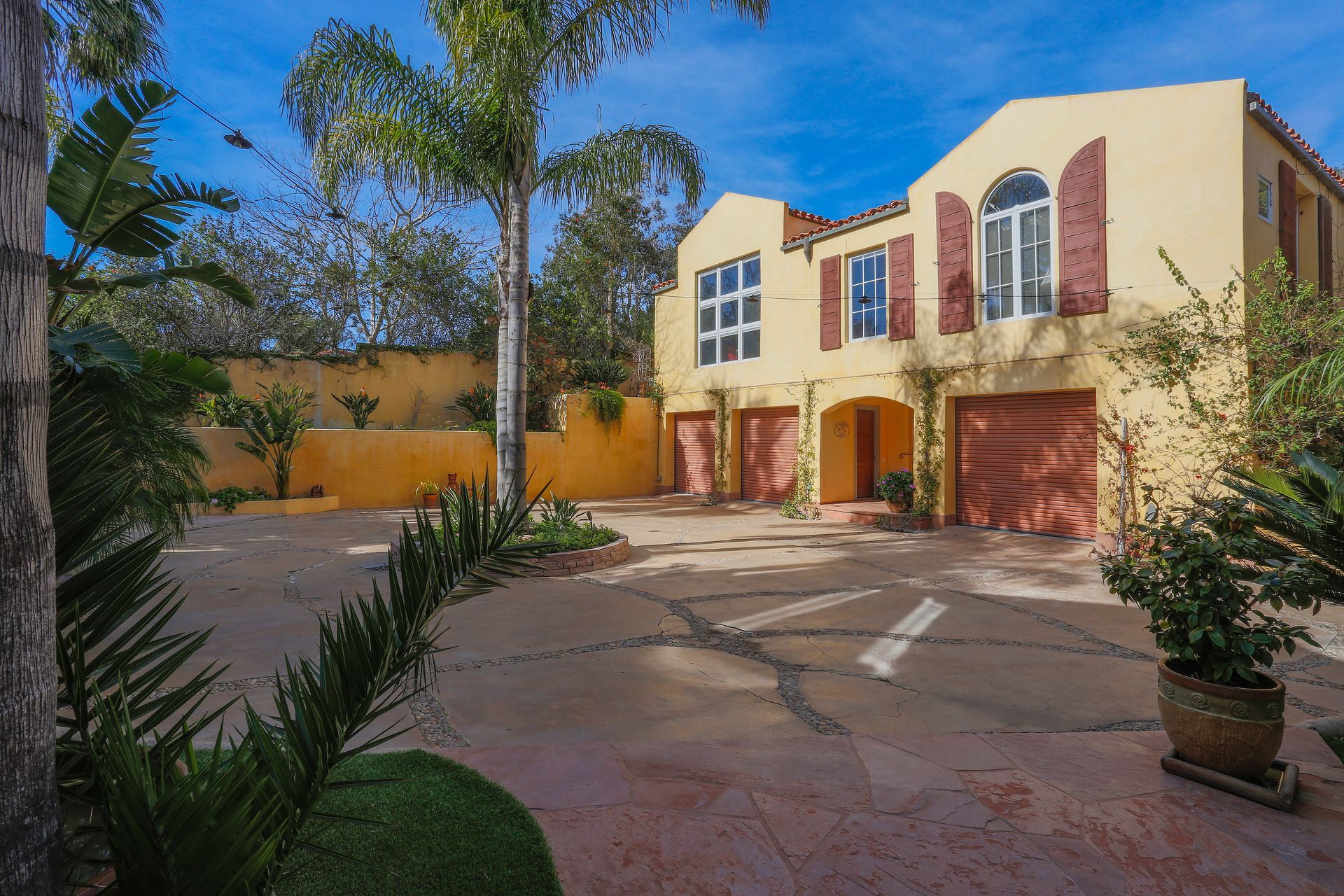 Sunlit Mediterranean-style house with red shutters, courtyard, and trees