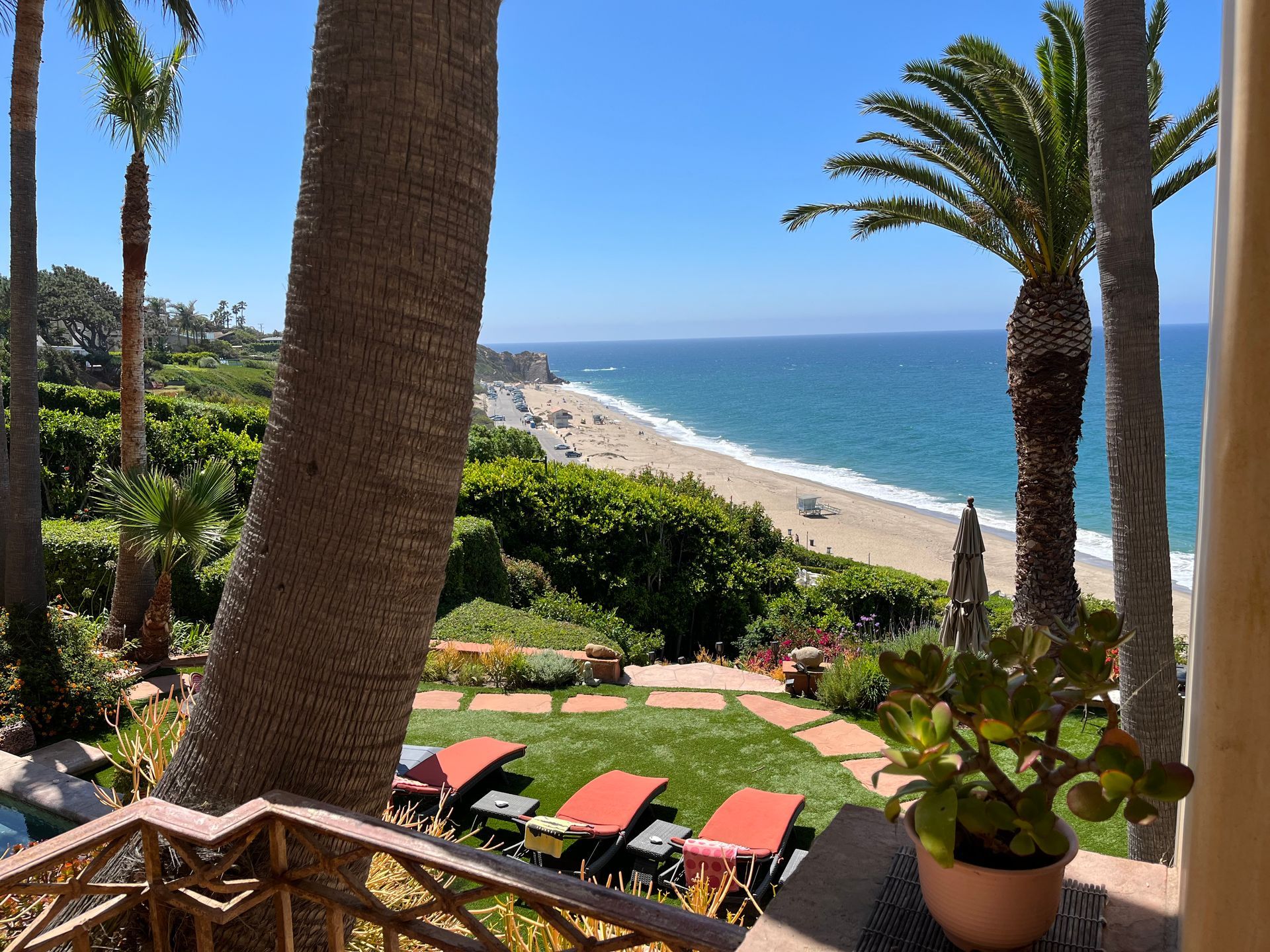 Oceanfront resort patio with palm trees, lounge chairs, and a beach and blue sea view