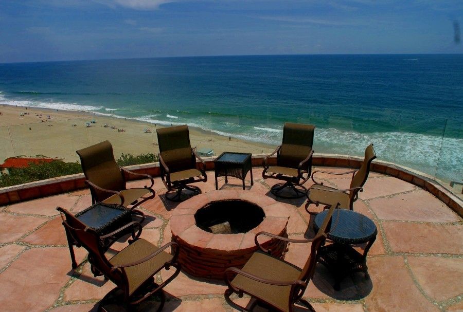 Patio chairs around a fire pit overlooking a sunny beach and ocean