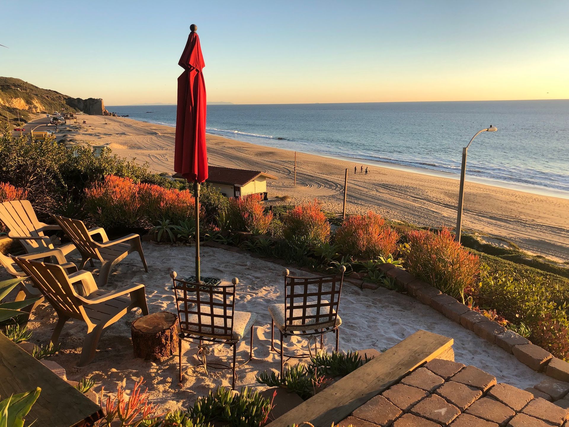 Patio overlooking a beach at sunset, with chairs, a red umbrella, and ocean view